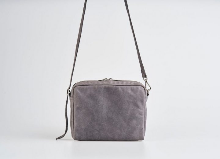 Product Picture front view of a standing up blue vegetable tanned leather small shoulder bag with a double silver zipper opening with a adjustable strap hanging straight in the air