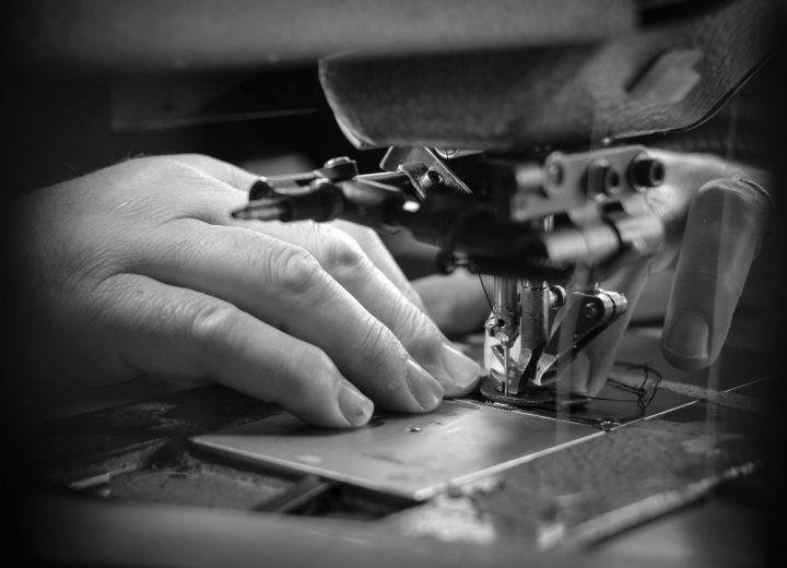 black and white picture of an closeup of a hand sewing with an industrial sewing machine