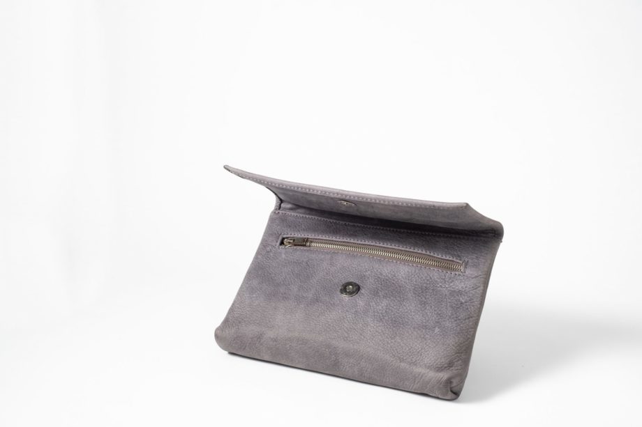 Front side view on an half standing blue-greyish vegetable tanned Leather Clutch with the flap half open so that you can see the magnetic button and a zip opening