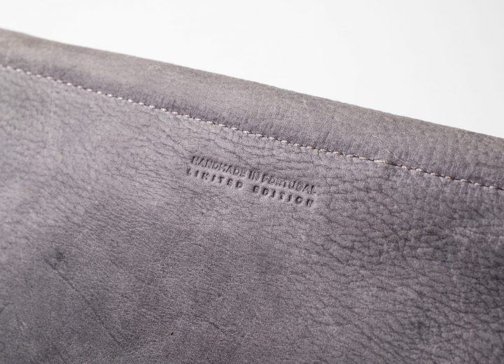 Zoom on the back of the blue-greyish vegetable tanned leather clutch showing one seam and a engraving saying "Handmade in Portugal, limited edition"